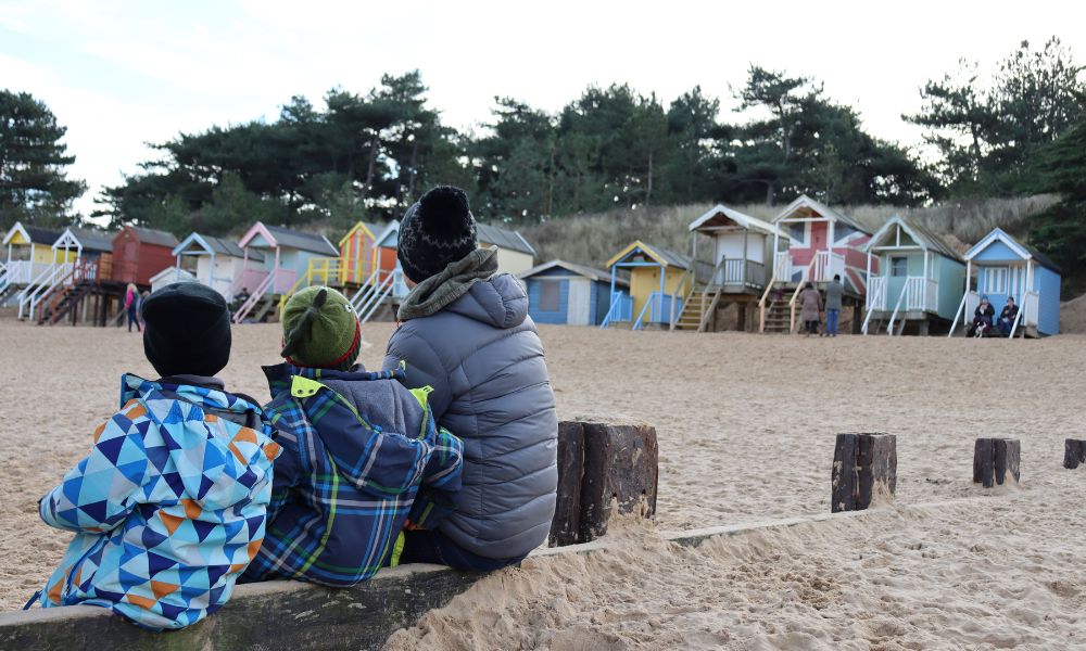 Family on family-friendly beach in Norfolk looking at colourful beach huts at Well-next-the-Sea.