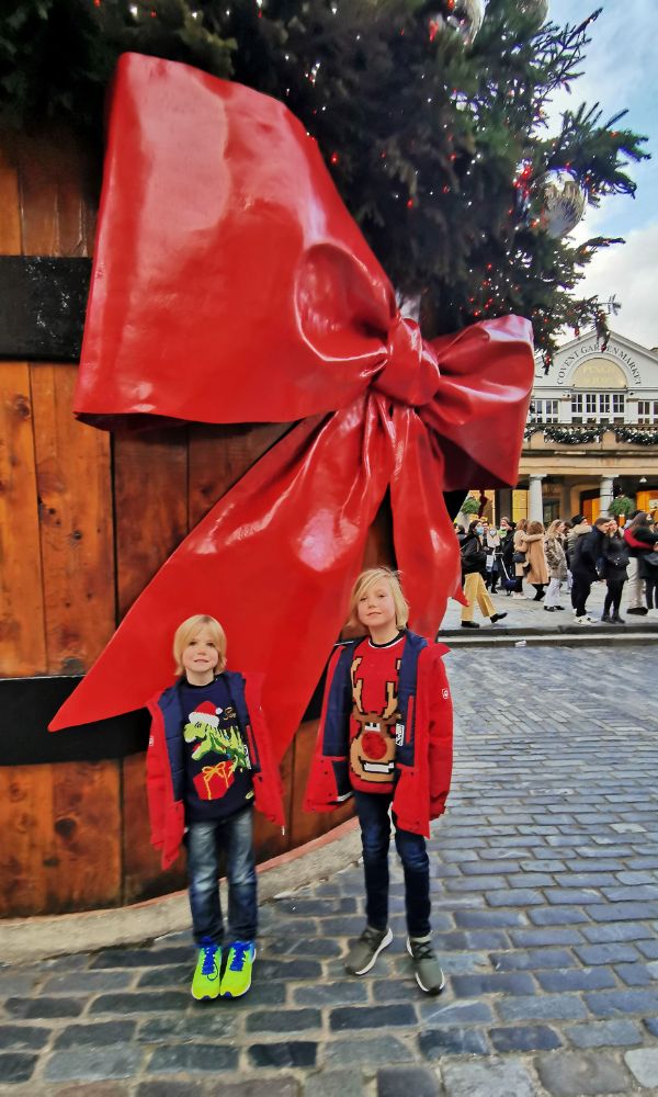Kids standing in front of a huge Christmas tree in Covent Garden in London at Christmas.