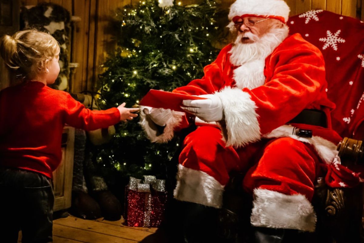 Little girl handing Santa a letter at the Santa's Grotto at Ribby Hall Village Christmas holiday for families.