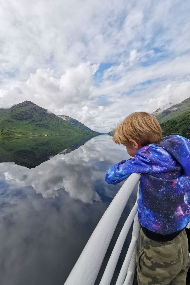 Child looking at the reflections in the water of the mountains and clouds at Loch Shiel in Scotland.