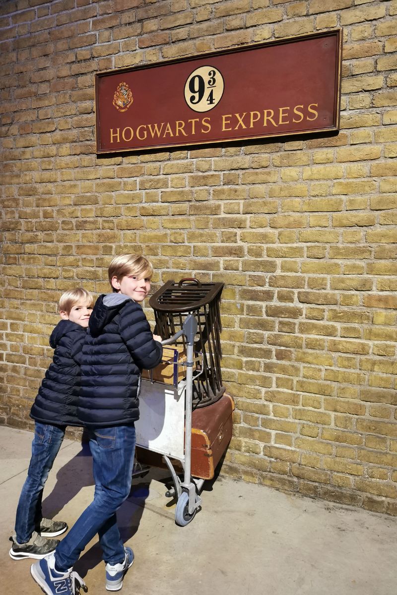 Kids trying to push the trolley through the wall on Platform 9 34 at Kings Cross in London.