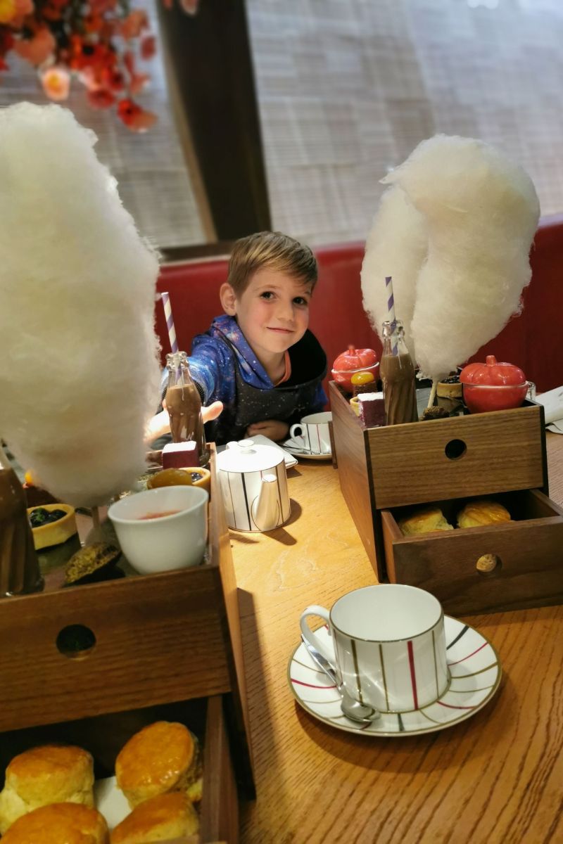 Boy reaching for a chocolate milkshake surrounded by candy floss at the Charlie and the Chocolate afternoon tea at One Aldwych.