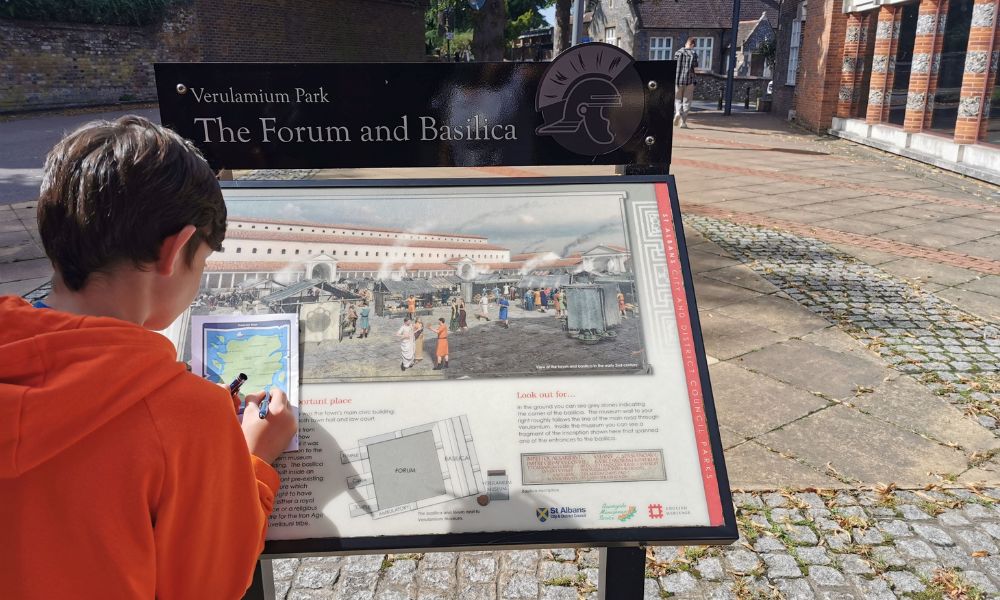 Boy standing in front of a sign for Verulamium Park in St Albans.