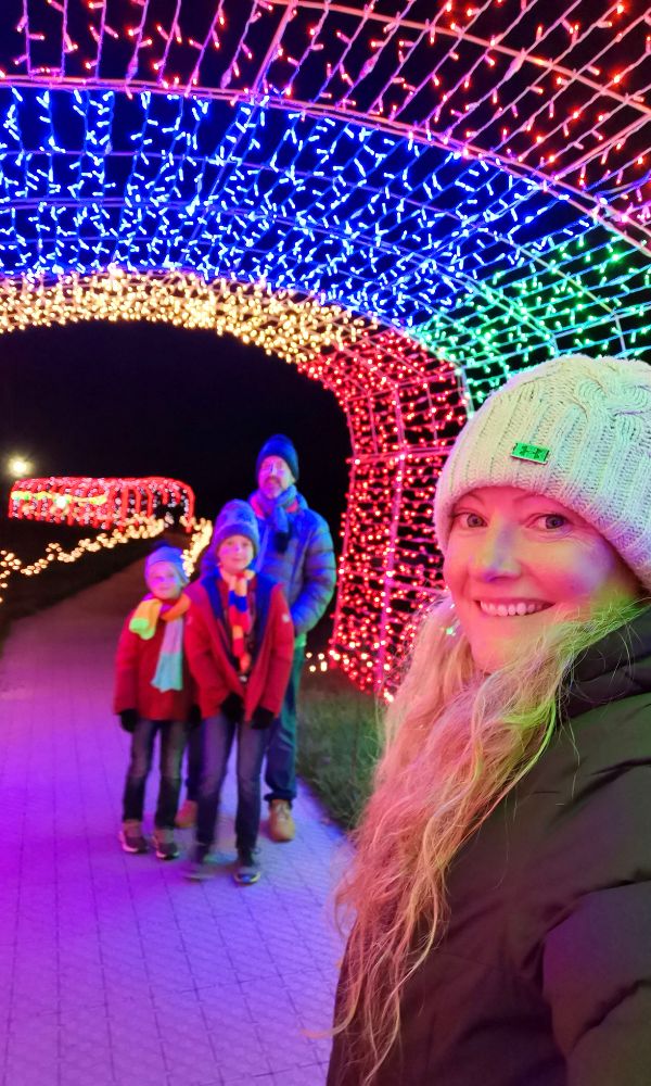Family taking a selfie in a colourful light tunnel during a Christmas light trail experience.
