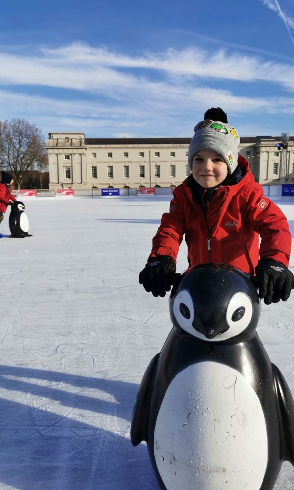 Kids ice skating at Christmas with a penguin skate aid.