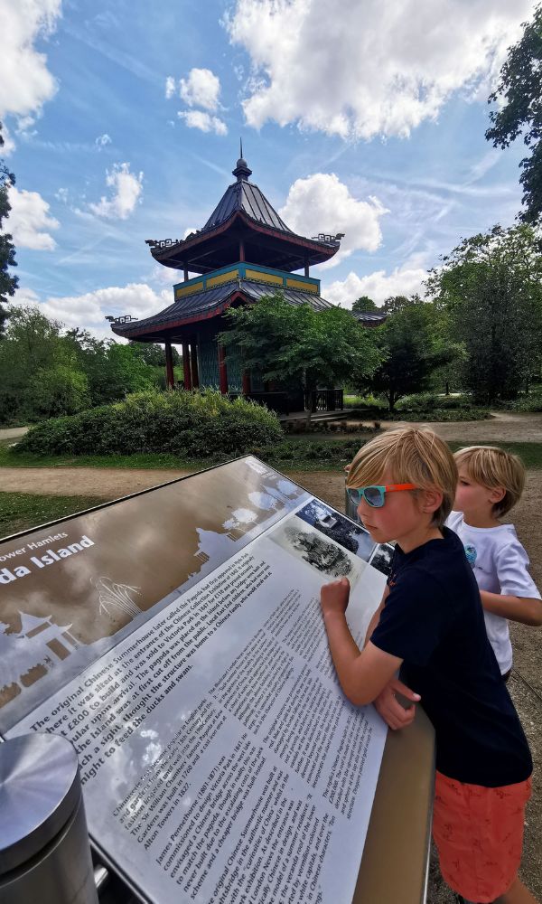 Kids in sunglasses reading the Pagoda Island information board in front of the Pagoda in Victoria Park in London.
