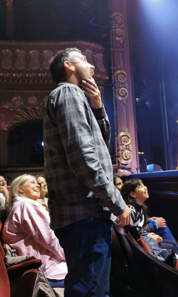 Man standing up in a theatre watching a Christmas Pantomime show.