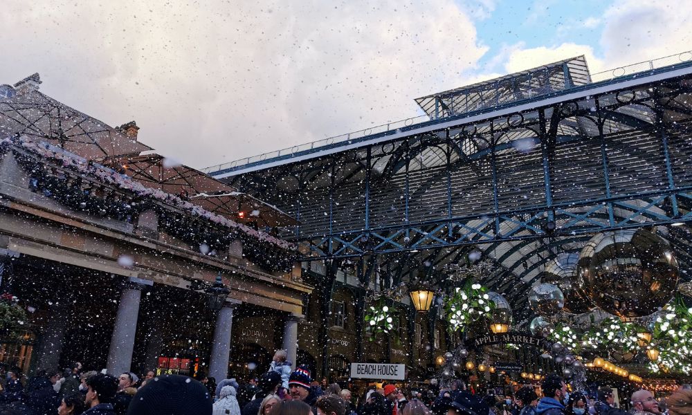 Snow falling on crowds of people at Covent Garden in London at Christmas.