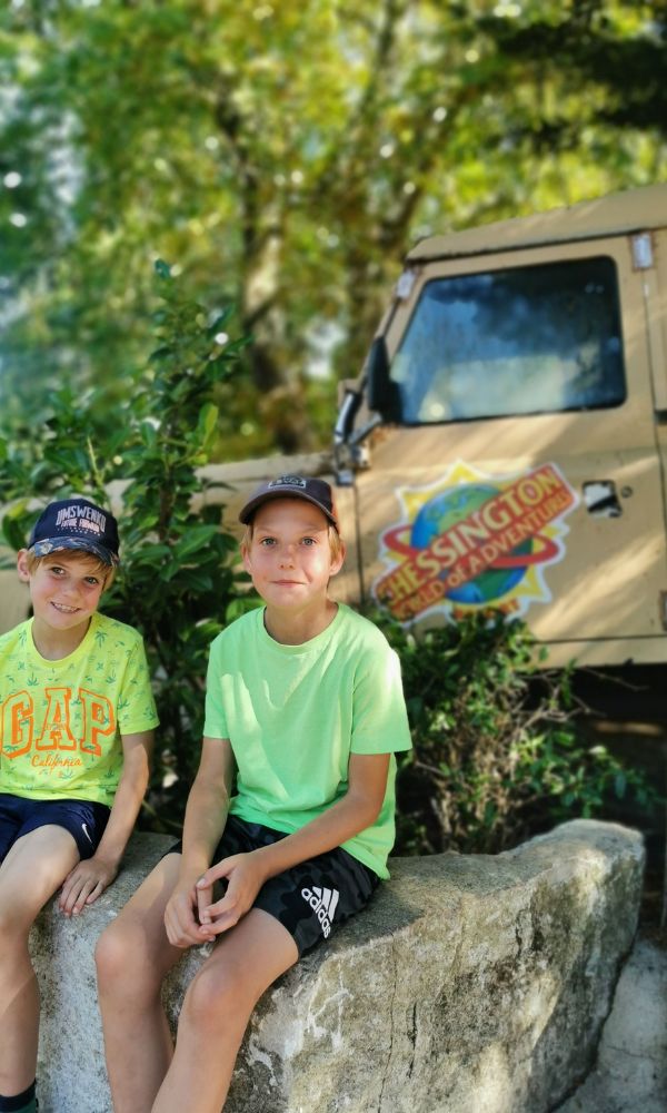 Two boys sitting in front of a jeep with the Chessington World of Adventures logo on it.