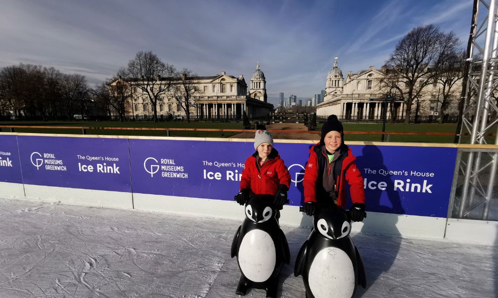 Two boys standing with penguin skate aids at Queen's House Ice Rink in Greenwich.