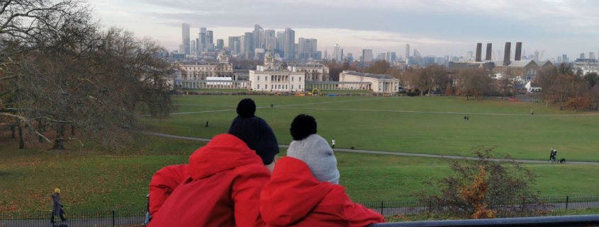 Two kids in red coats looking at one of the best free views of the London skyline from Greenwich Park.