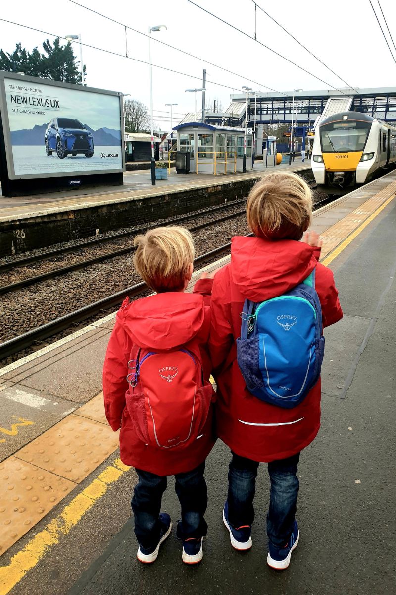 Two kids on a train station platform with a train approaching.