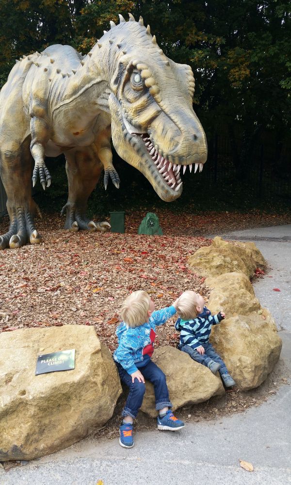 Two toddlers looking up at a life sized T-Rex.