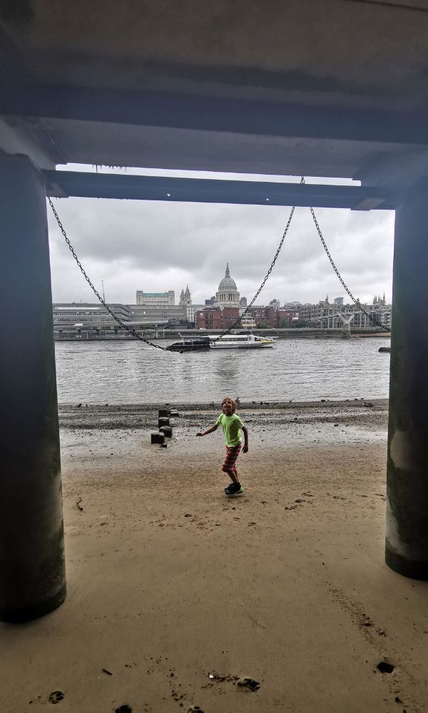 Young boy walking alongn the banks of the River Thames in London at low tide.