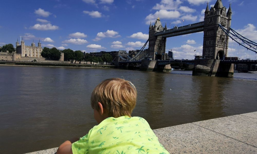 Young boy in a yellow tshirt looking across the River Thames at the Tower of London and Tower Bridge.