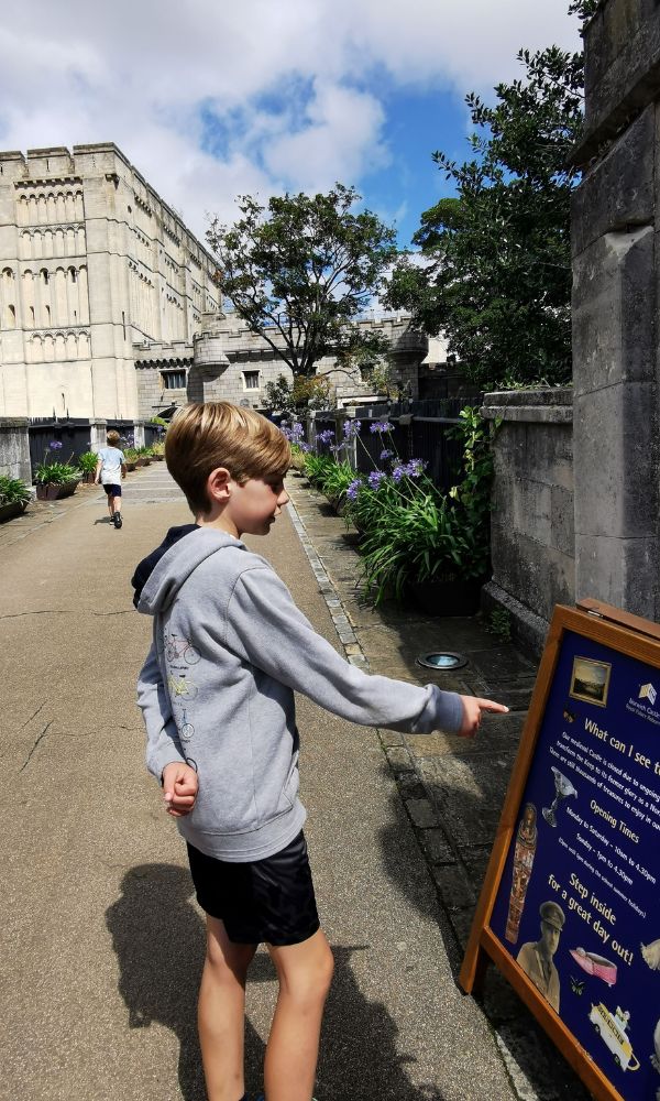 Boy looking at a notice board showing what's on at Norwich Castle with Norwich Castle in the background.